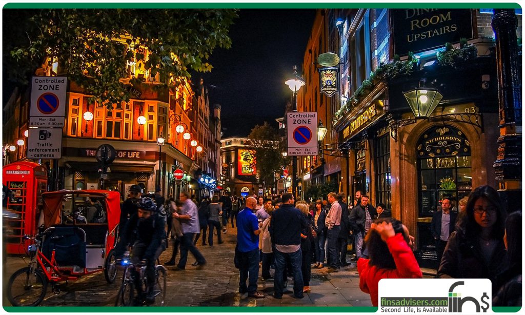 نمایی از شلوغی خیابان های لندن در شب در صورتی که زن و مردان جوان دور هم جمع شده اند- زندگی در لندن
