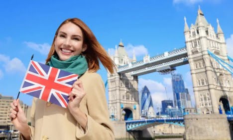 دختری با موهای خرمایی در شهر لندن با لبخند عکس پرچم انگلیس را در دست گرفته است ـ جاب آفر انگلیس