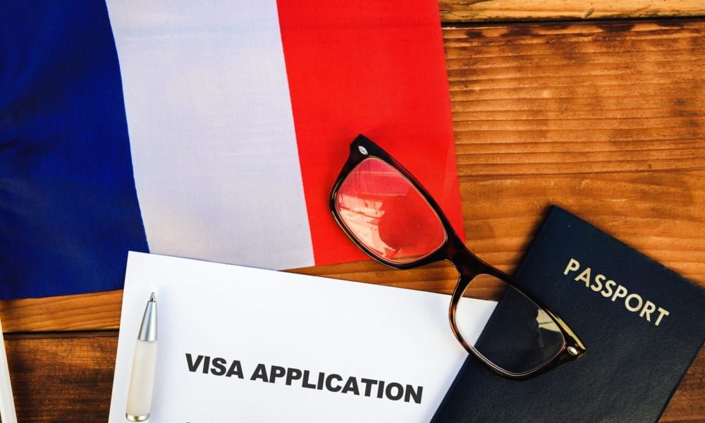 عکس یک میز که بر روی آن یک پرجم از اسپانیا و پاسپورت و یک عینک است - شرایط ویزای تمکن مالی فرانسه